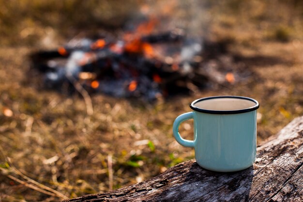 Focused blue cup of coffee and burned out campfire