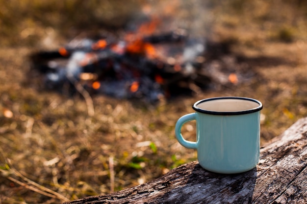 Focused blue cup of coffee and burned out campfire