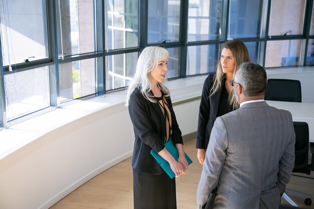 Focused business group standing and talking in office, talking, discussing project and work issues. Copy space. Business communication or briefing concept