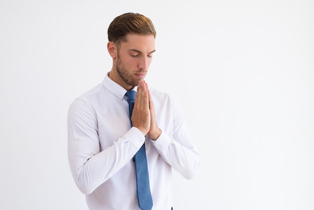 Focused business man praying and keeping hands together.