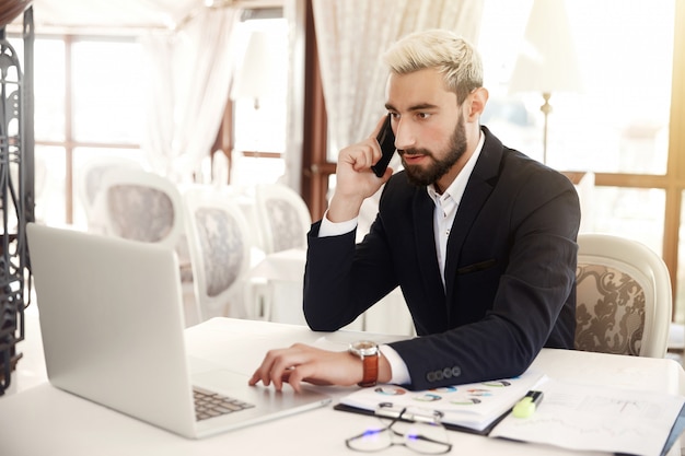 Foto gratuita l'uomo d'affari messo a fuoco sta guardando sullo schermo di un computer portatile e sta parlando sul cellulare