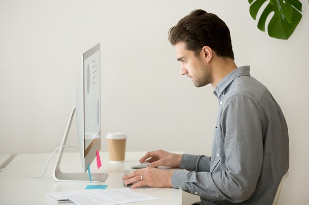 Сосредоточенный бизнесмен работает на компьютере со статистикой проекта, вид сбоку