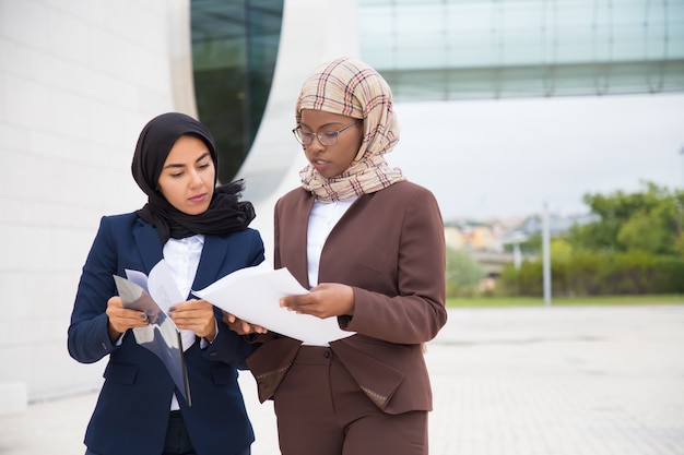 Free photo focused businesswomen walking on street and inspecting documents