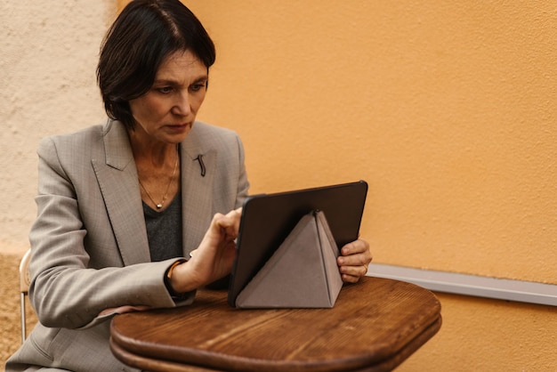 Free photo focused caucasian adult brunette woman is using tablet at table in open air fashion technology and people concept