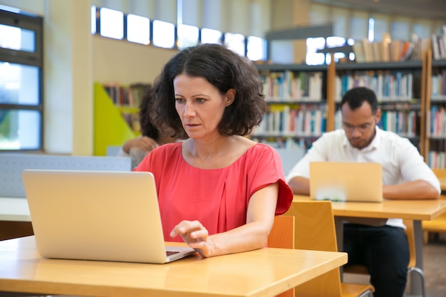 Focused Caucasian woman looking at laptop while sitting at table