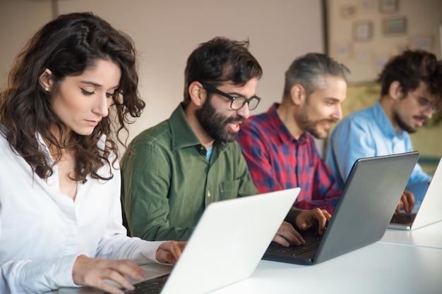 Focused coworkers using laptops at meeting table