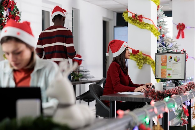 Бесплатное фото Сосредоточенные сотрудники исследуют ключевые данные для проекта компании во время рождественских праздников многонациональная бизнес-команда решает задачи в празднично украшенном офисе до приближения крайнего срока