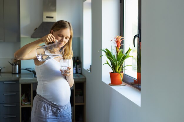 Focused expectant mother holding jug and glass