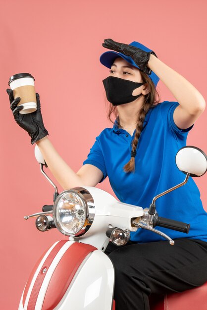 Focused female courier wearing black medical mask and gloves delivering orders on peach background