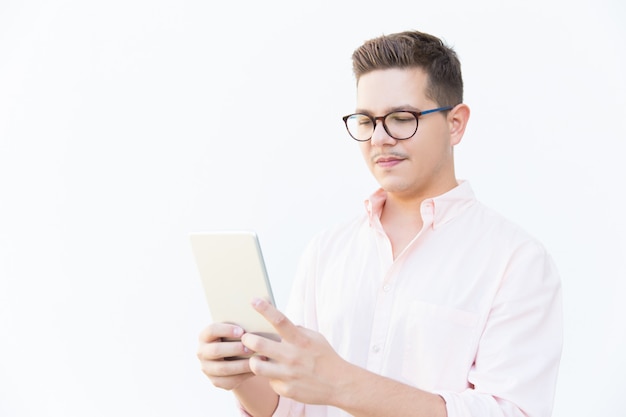 Сосредоточенный парень в очках читает на экране планшета