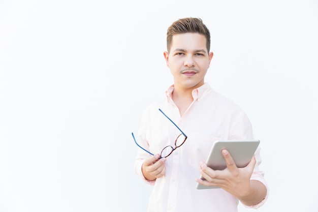 Focused guy holding eyeglasses and tablet