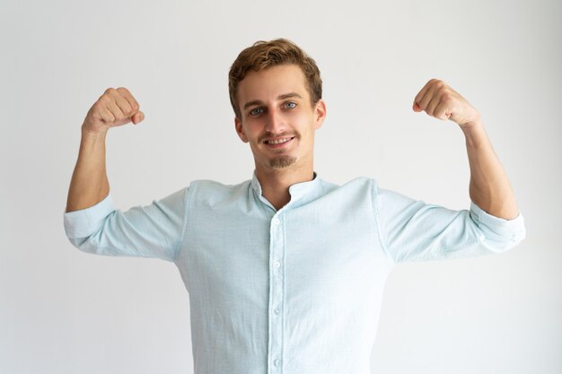 Focused guy in white casual shirt showing strength gesture. 