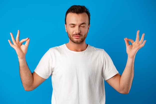 Focused handsome young man meditating on camera iover blue background