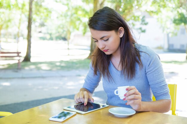 コーヒーを飲みながら、屋外カフェでタブレットを使用して女性に焦点を当ててください。