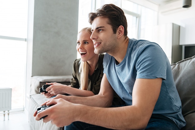 Focused lady and man playing video games at home in living room