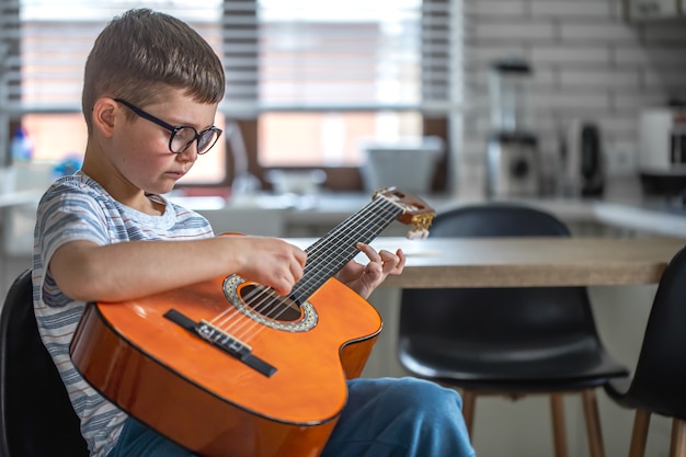 自宅のキッチンでギターを片手に座っている集中力のある小さな男の子。