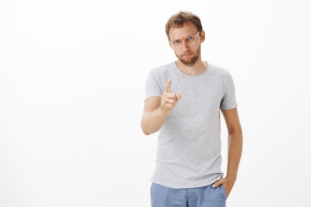 Focused male entrepreneur giving directions on duty being strict and serious with employees shaking index finger, pointing, dissatisfied or disappointed with bad work over white wall