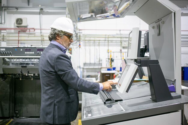 Сосредоточенный мужчина-менеджер завода, работающий на промышленной машине, нажимая кнопки на панели управления