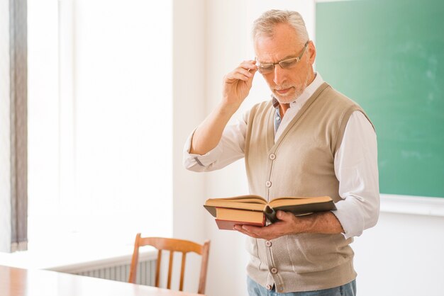 focused male professor in glasses reading book in classroom