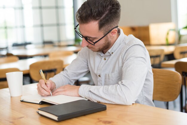 Focused male student writing in notebook at desk in classroom