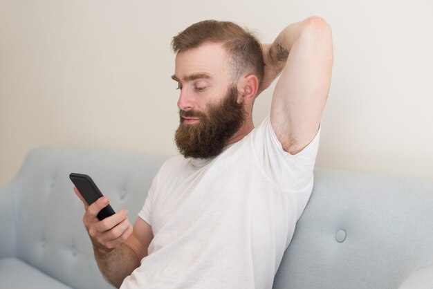 Focused man browsing on smartphone and sitting on sofa