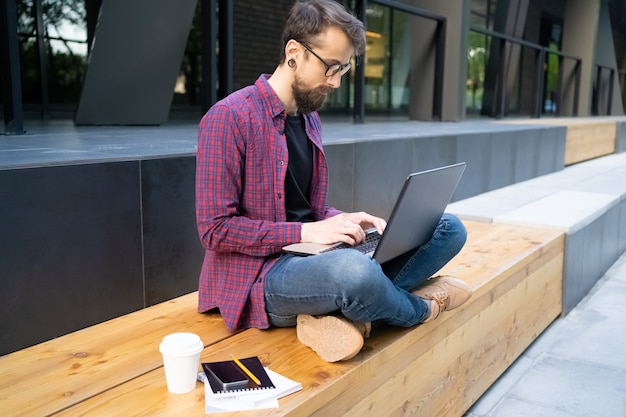 Focused man sitting cross-legged on wooden bench with laptop