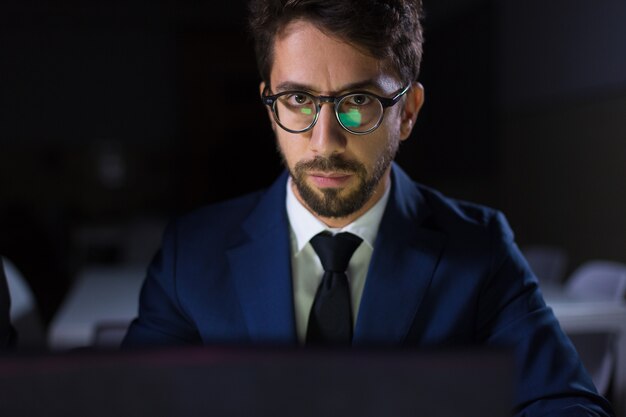 Focused man sitting at table with laptop and looking at camera