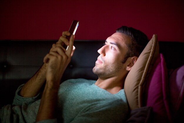 Focused Man Using Smartphone on Sofa at Night