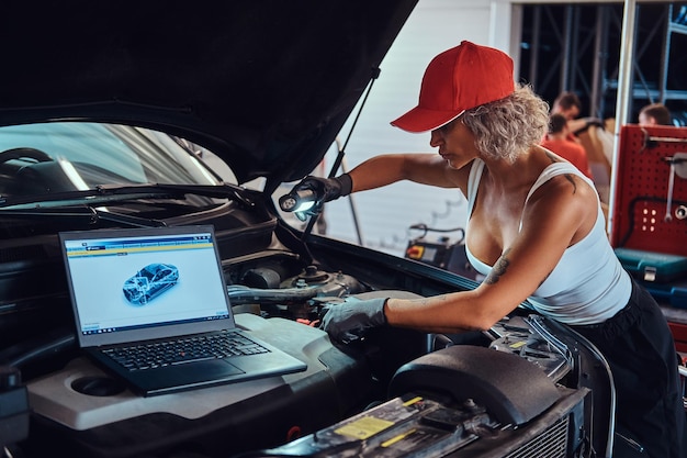 Сосредоточенная мужественная женщина занимается диагностикой автомобиля с помощью компьютера в автосервисе.