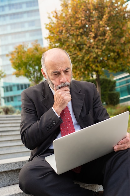 Focused mature businessman using laptop outdoors