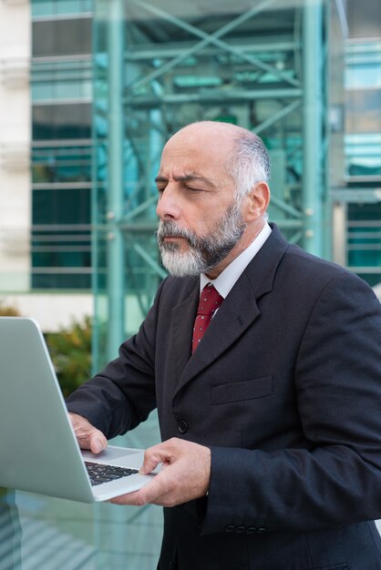 Сосредоточенный зрелый бизнесмен с ноутбуком, проверка электронной почты