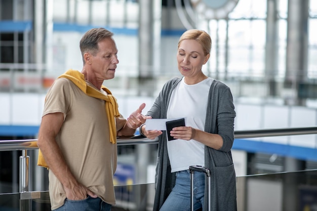 Focused middle-aged Caucasian male passenger pointing at the boarding ticket in his female companion hands