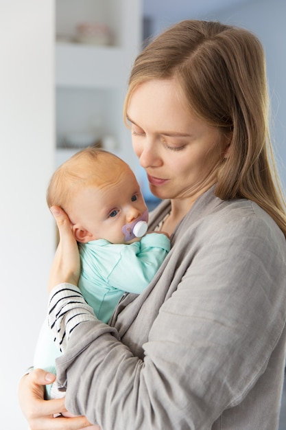 Focused new mother cuddling baby with soother