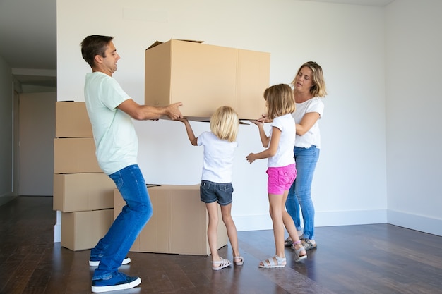 Focused parents and two girls carrying boxes into new empty flat together