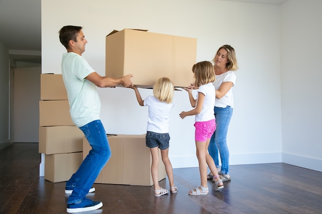 集中した両親と2人の女の子が一緒に新しい空のアパートに箱を運ぶ