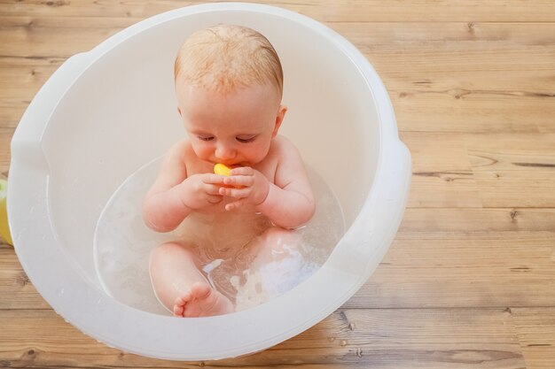 집에서 욕조에 목욕하는 동안 노란색 고무 장난감 오리를 물고 달콤한 젖은 아기를 집중했다. 근접 촬영. 육아 또는 건강 관리 개념