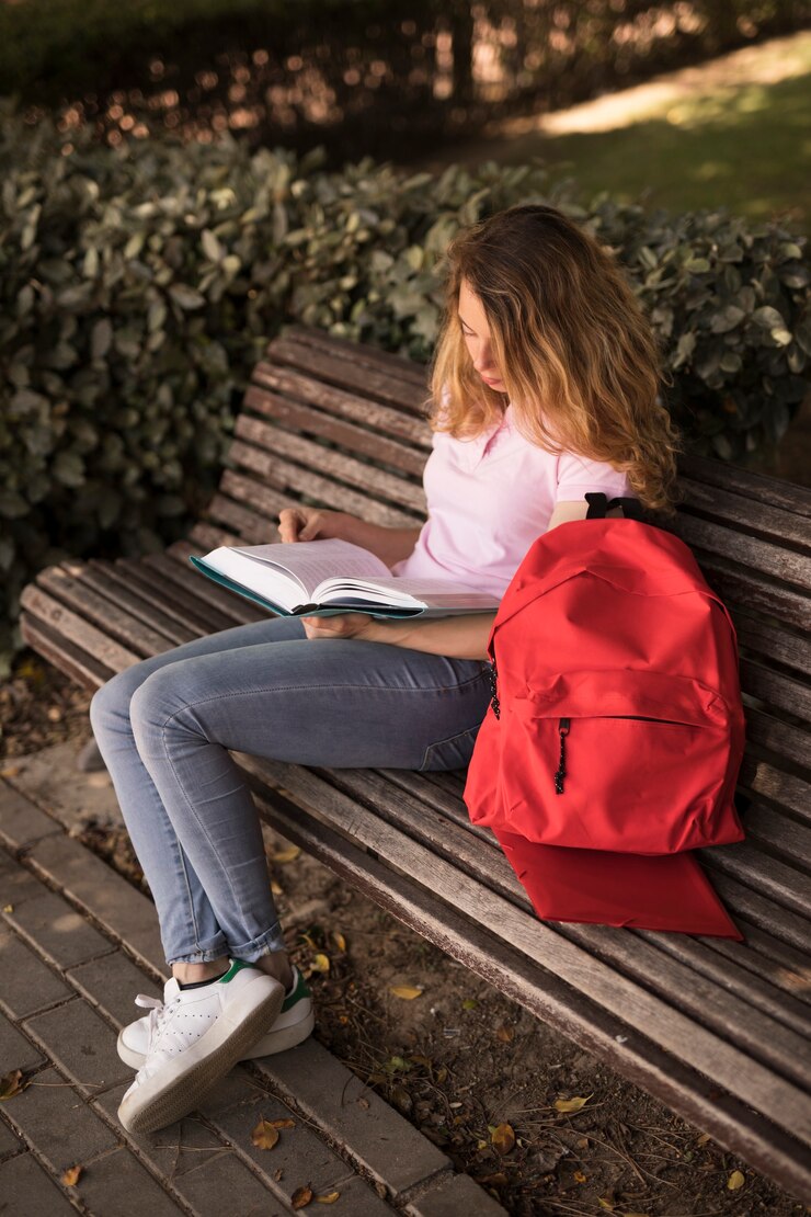 Free Photo focused teen woman reading workbook on bench