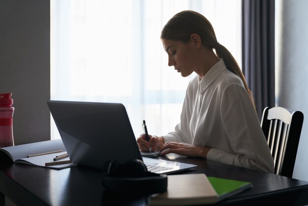 Focused woman sitting at table and working on laptop