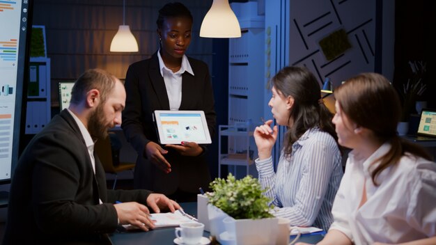 Focused workaholic african american businesswoman showing financial graphs on tablet