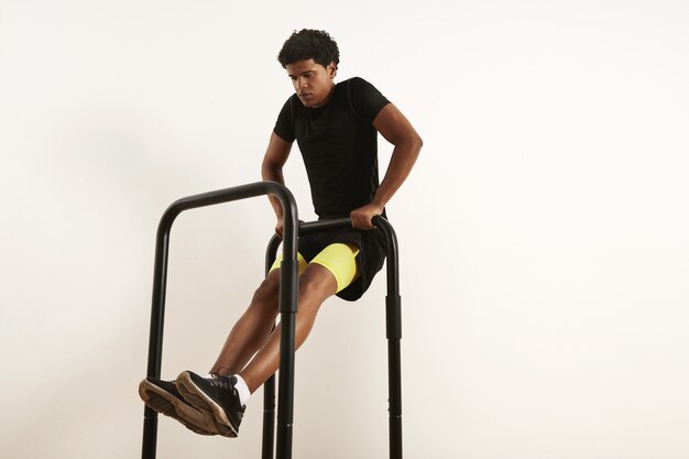 Focused young African American athlete in black sportswear performing bodyweight rows on mobile bars isolated on white