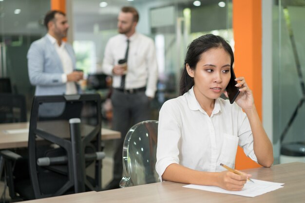 Focused young Asian business woman talking on phone and working