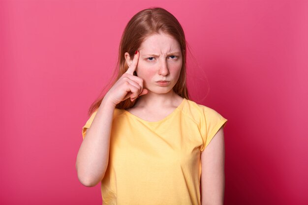 focused young Caucasian girl touching temples with index fingers and frowning, has pensive facial expression