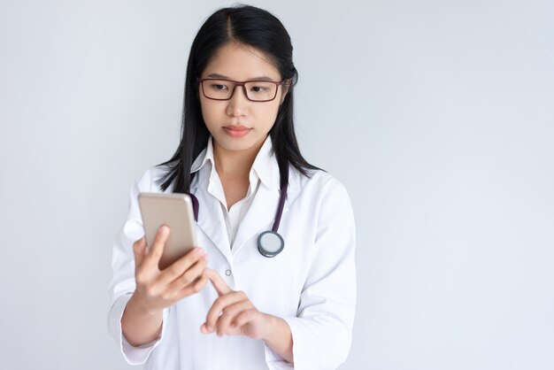 Focused young female doctor using smartphone