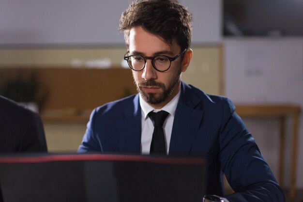 Free photo focused young man in eyeglasses looking at laptop