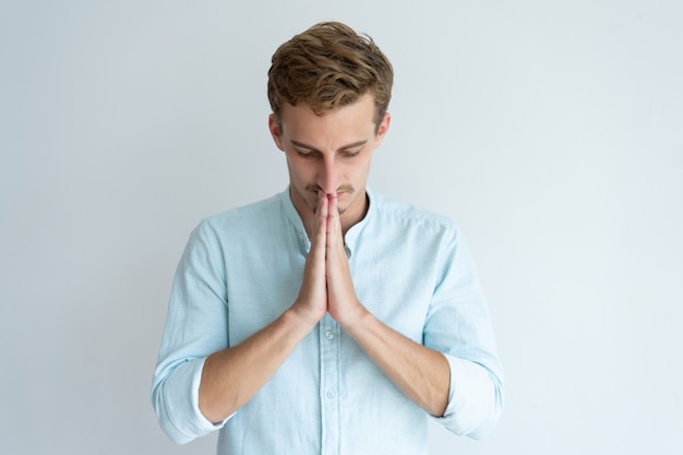 Сосредоточенный молодой человек молится и держит руки вместе. Гай просил у Бога чего-то.
