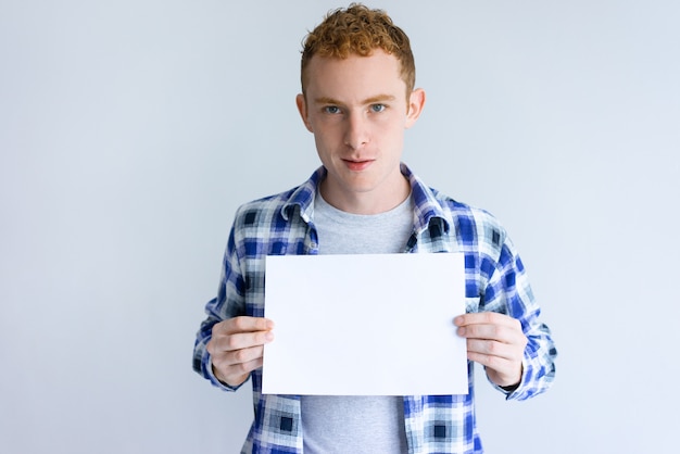 Free photo focused young man showing blank sheet of paper