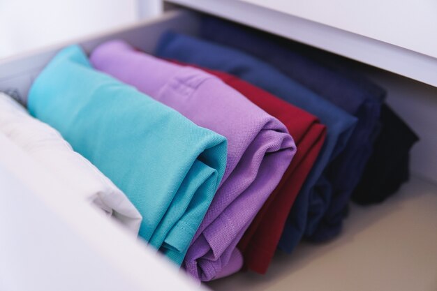 Сложенная разноцветная одежда разложена в шкафу под светом
