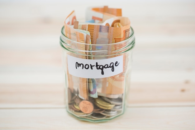 Folded euro notes and coins in the mortgage glass jar on wooden backdrop