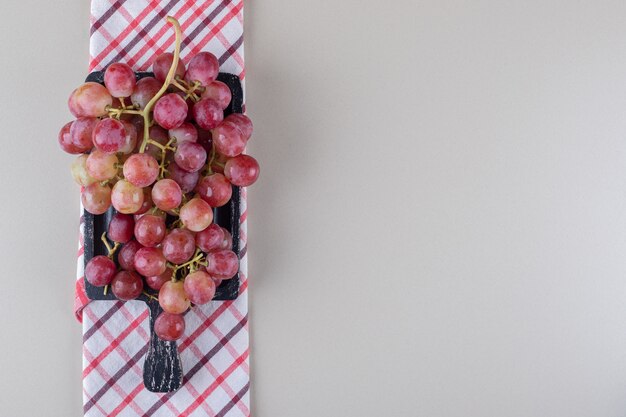 Folded towel under a small tray with red grapes on marble 