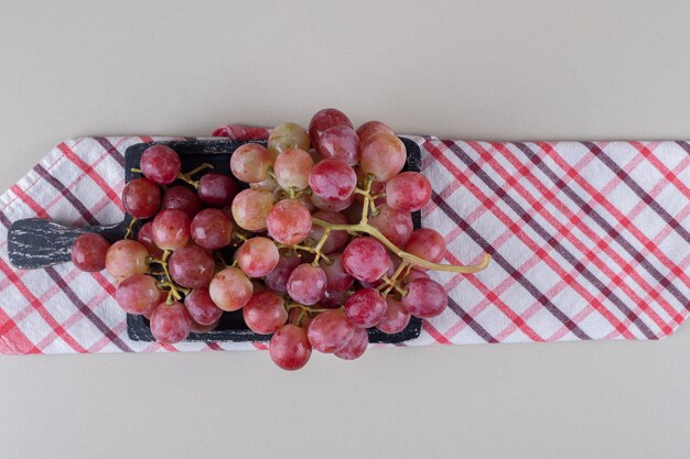 Folded towel under a small tray with red grapes on marble 